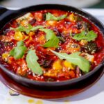 Freshly prepared vegetable stew garnished with arugula, served in a black skillet.