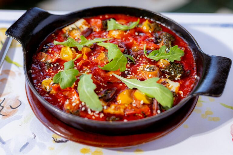 Freshly prepared vegetable stew garnished with arugula, served in a black skillet.